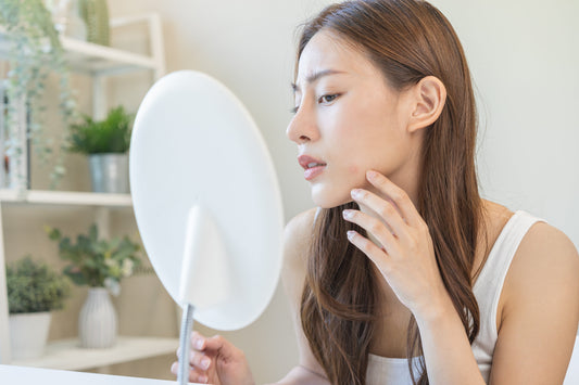 A woman looking at acne pimple in vanity mirror