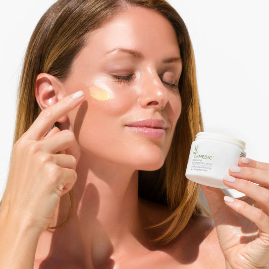 Woman applying ORMEDIC® Balancing Biopeptide Crème to her face for hydration and luminous skin.