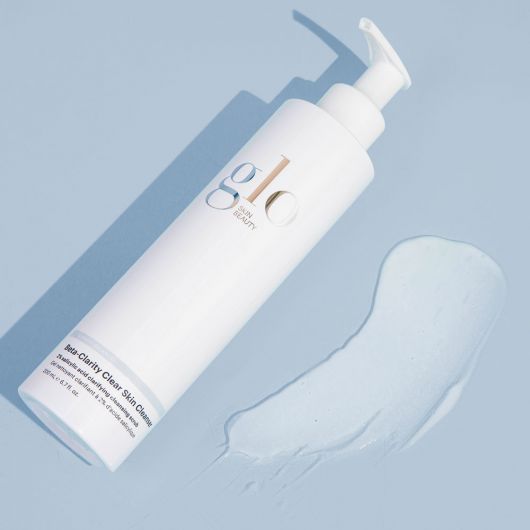 Beta-Clarity Clear Skin Cleanser bottle with pump next to a spilled liquid on a blue background.