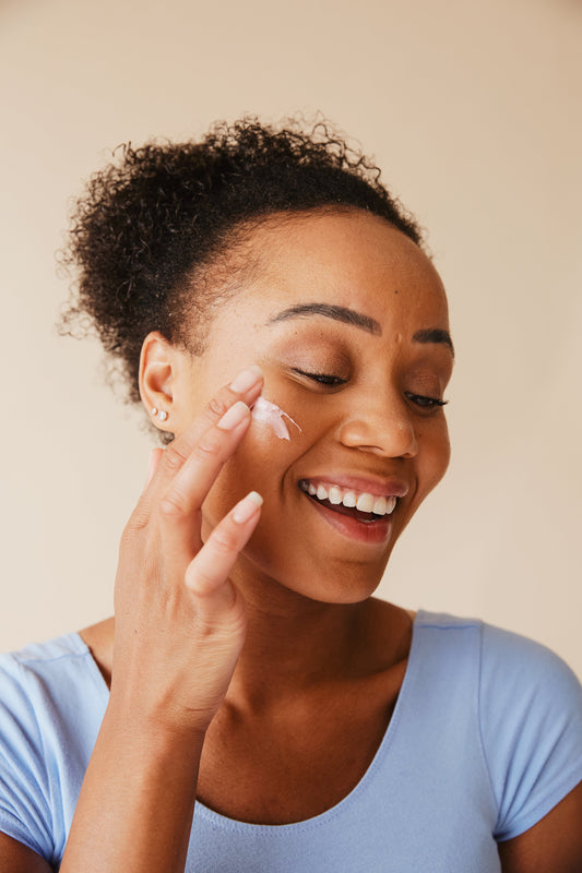 Woman applying sunscreen to her face, smiling and promoting healthy skin care practices.