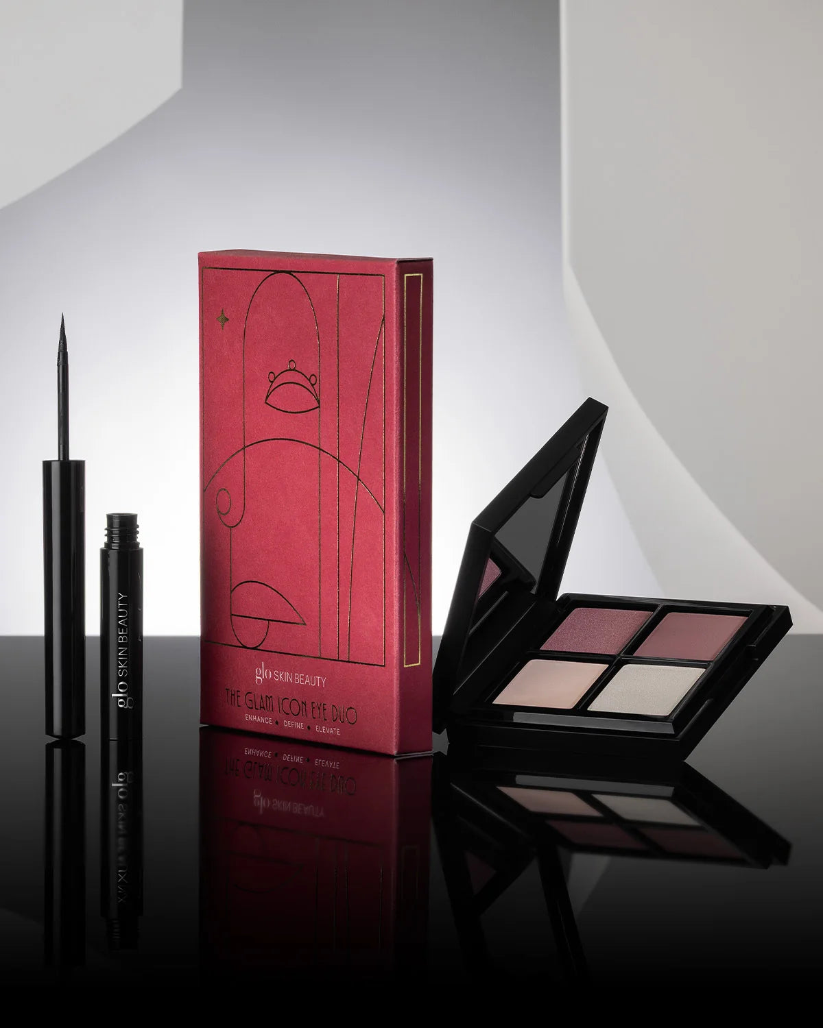 The Glam Icon Eye Duo featuring a silver and smoke shadow quad and Precision Liquid Eyeliner on a reflective surface.