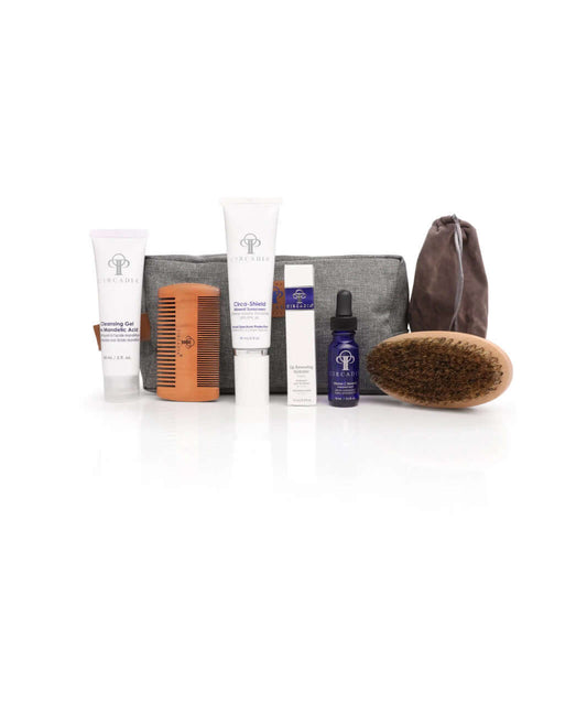 Gentleman's Regimen Bundle including luxury grooming products: cleansing gel, vitamin C serum, sunscreen, lip hydrator, beard brush/comb, and gray toiletry bag.