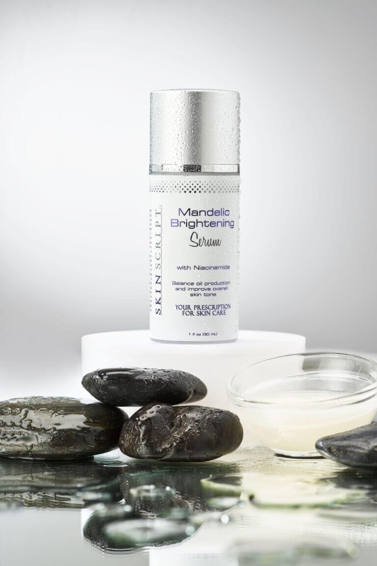 Mandelic Brightening Serum with Niacinamide bottle on display with pebbles and glass dish in a skincare setting.