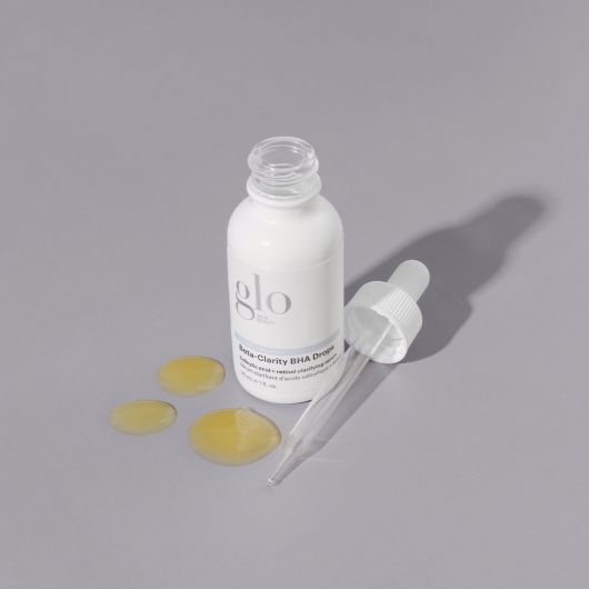 Beta-Clarity BHA Drops serum bottle and dropper with liquid on a gray background for clear, smooth skin, featuring retinol, glycolic, and salicylic acid.