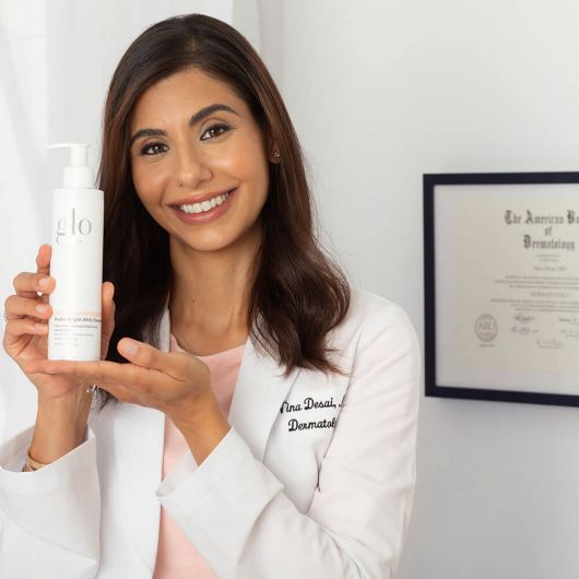 Certified dermatologist holding Hydra-Bright AHA Cleanser for hydrating and brightening skincare routine