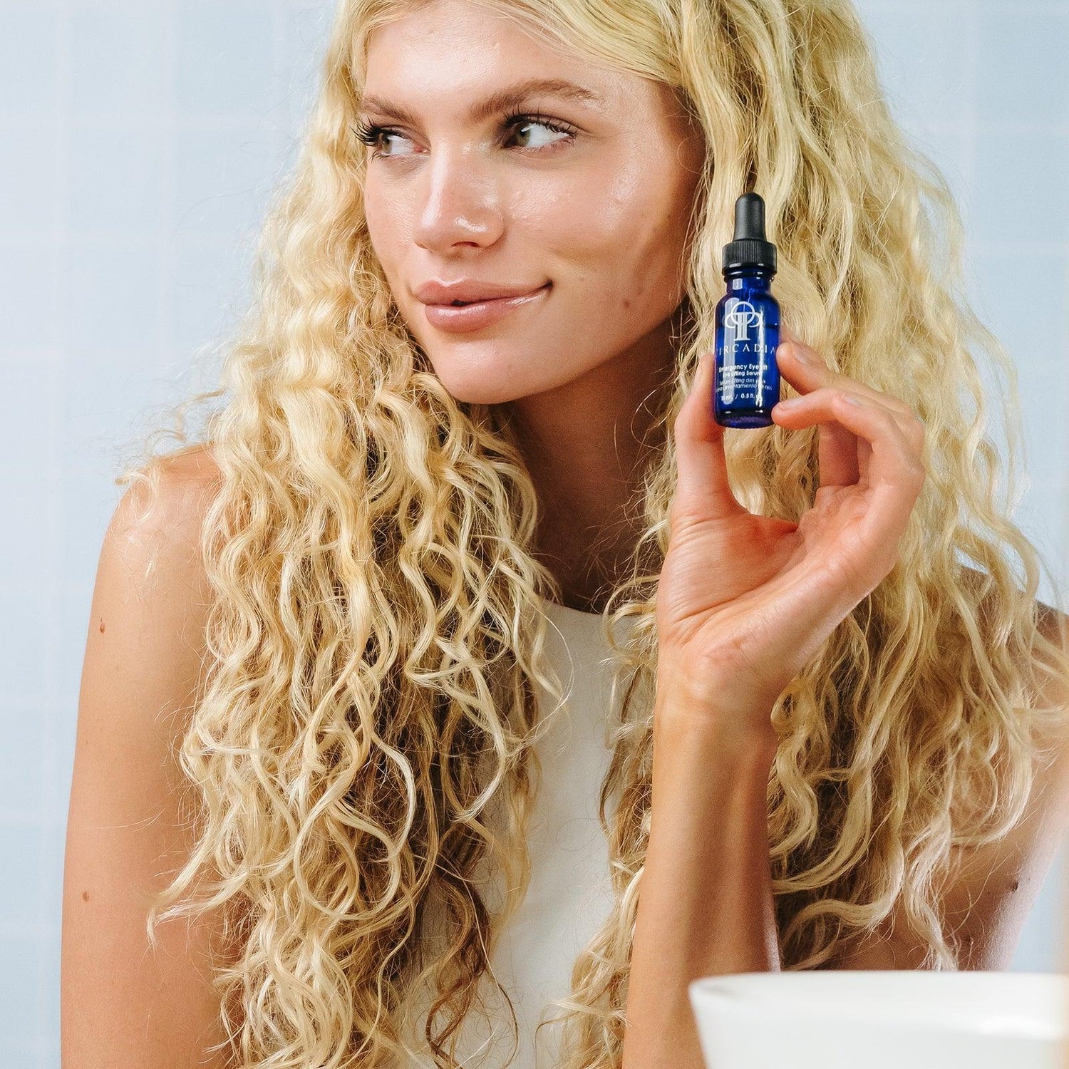 Model showcasing Circadia Emergency Eye Lift gel with a clear blue bottle, promoting eye area lifting and tightening.