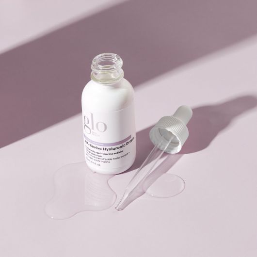 HA-Revive Hyaluronic Drops bottle and dropper on a light pink surface, showcasing the hydrating serum's packaging and texture.