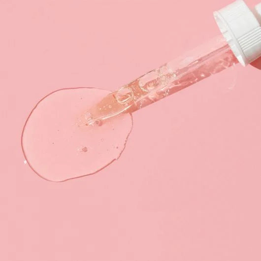 Hydra-Bright Vitamin C Drops serum dropper against a pink background, showcasing the clear, powerful brightening serum.