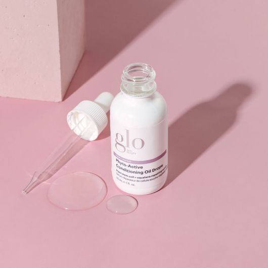 Phyto-Active Conditioning Oil Drops bottle with dropper, displayed on a pink surface, featuring skin-rejuvenating plant stem cell technology.