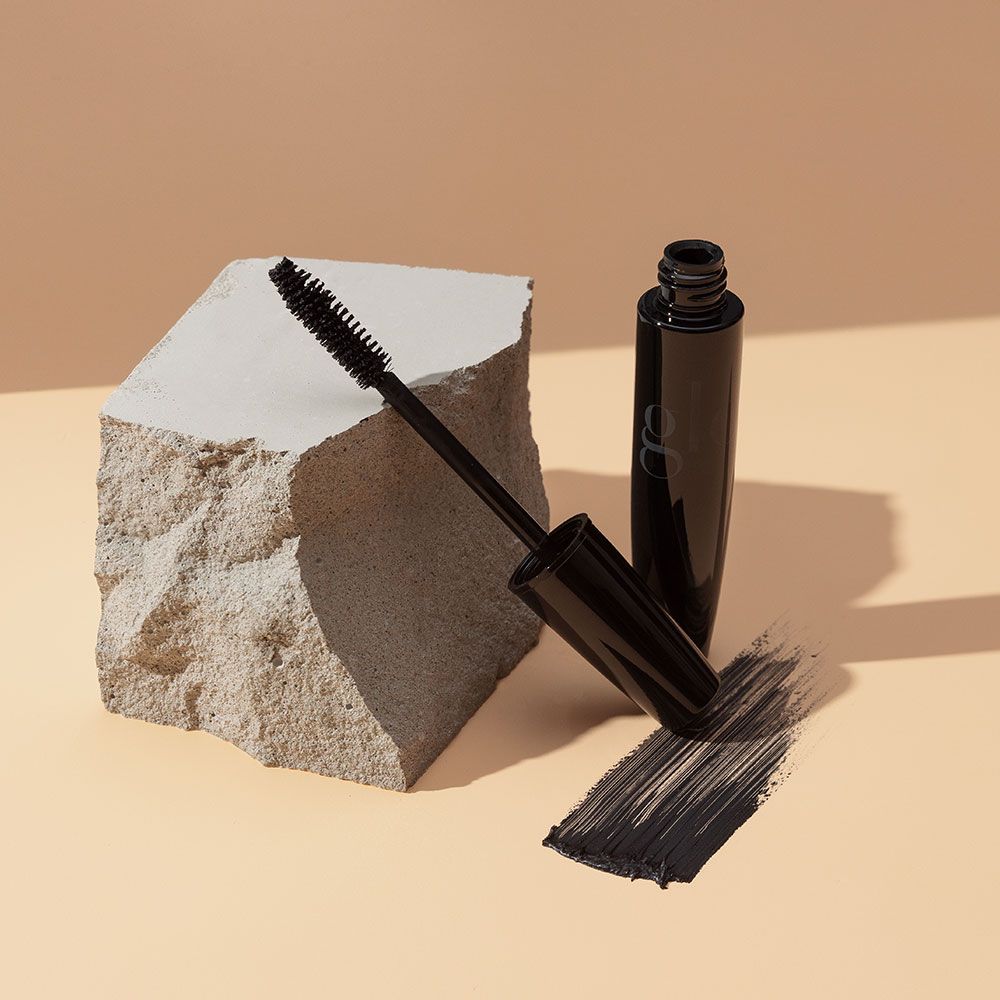 Volumizing Mascara with pro full-body brush open next to a smudge, displayed on a beige rock background.